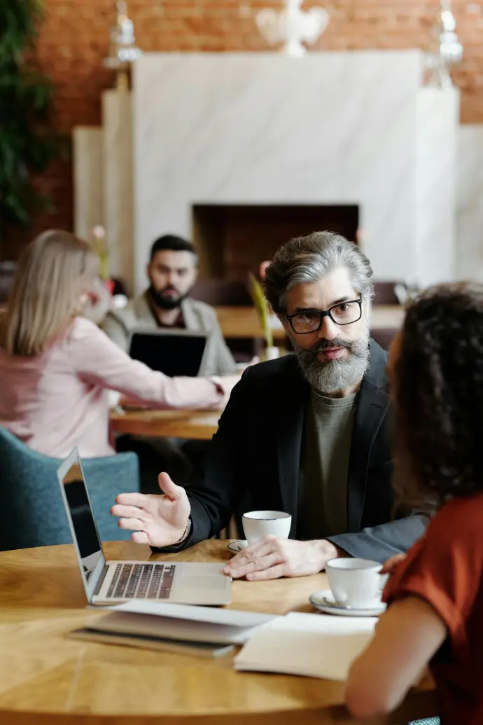 A man with glasses and a beard converses with a woman at a table about online business growth.